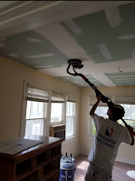 A man is painting the ceiling of a room with a vacuum cleaner.
