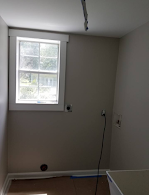 A laundry room with a window and a trash can.