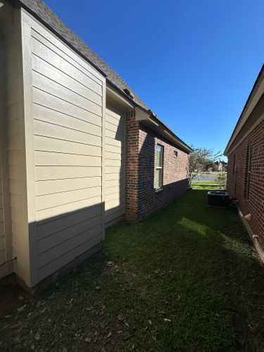 The side of a house with a brick wall and a white siding.