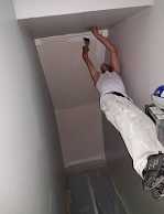 A man is hanging upside down from the ceiling while painting a wall.