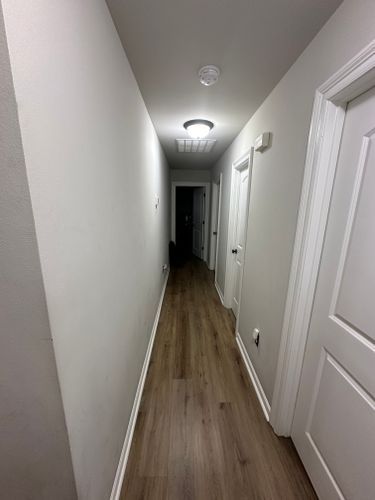 A long hallway with hardwood floors and white walls in a house.