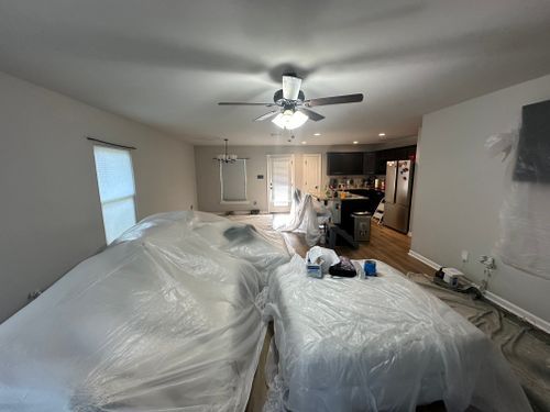A living room with a ceiling fan and two beds covered in plastic.