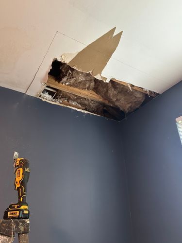 A room with a hole in the ceiling and a drill on a ladder.