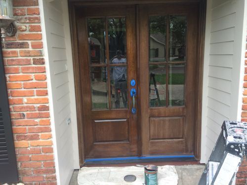 A man is painting the front door of a brick house.