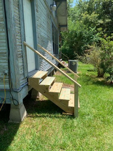 A wooden staircase is sitting in the grass next to a house.