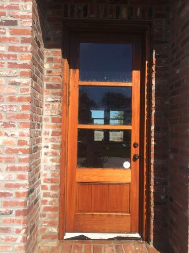 A wooden door with a glass window is on a brick building.