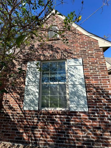 A brick house with a window and white shutters on it.