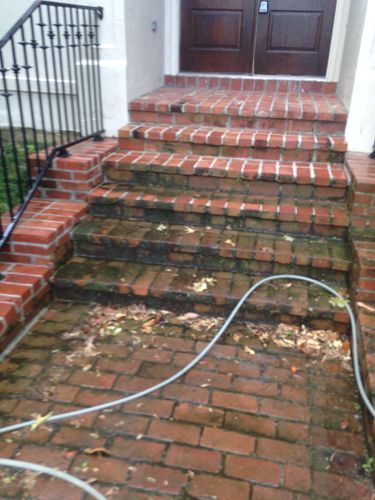 A hose is sitting on a brick walkway next to a set of stairs.