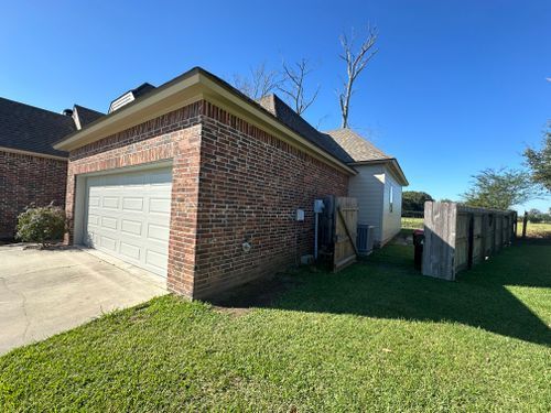 A brick garage with a white door is in the backyard of a house.