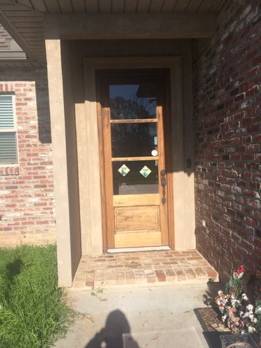 The front door of a brick house with a wooden door and a glass door.