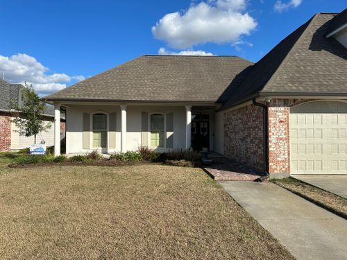A white house with a gray roof and a brick wall is for sale.