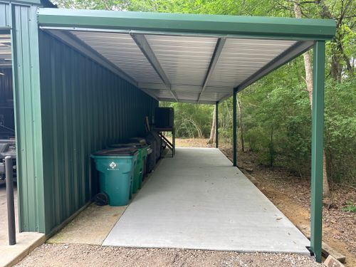 A green metal carport with trash cans underneath it.