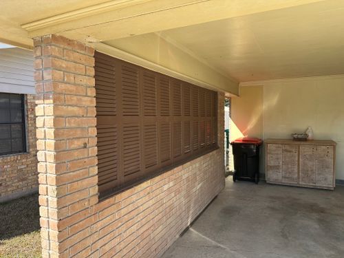 A brick wall with shutters on it and a trash can in the background.