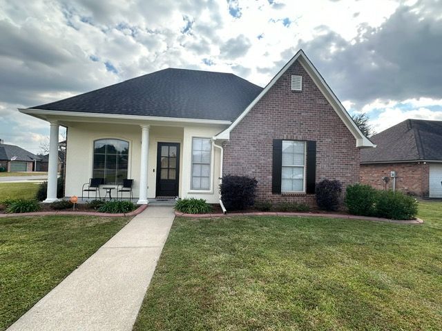 House exterior with brick and stucco, black roof, white columns, lawn, cloudy sky.