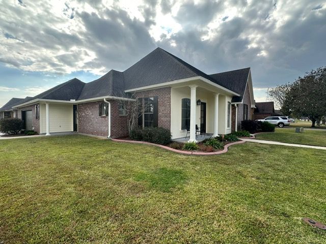A house with a dark roof and white trim. It has a brick facade with a green lawn. Cloudy sky.