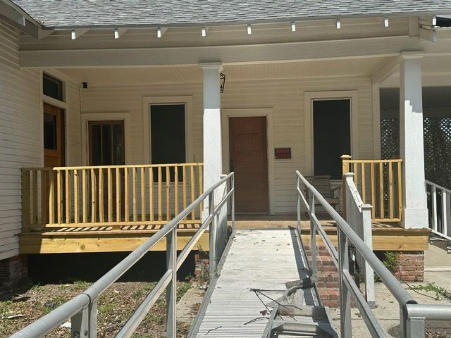 White building with a porch, a wheelchair ramp, and a wooden railing.