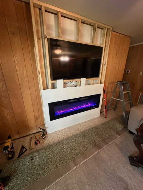 Fireplace installation: TV mounted above electric fireplace, framed in wood on paneled wall.