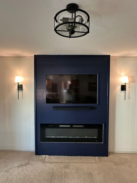 Navy blue accent wall with TV, soundbar, electric fireplace, sconces, and overhead light.