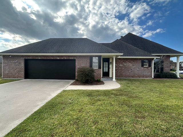 Single-story brick house with black garage door, dark roof, and green lawn under a cloudy sky.