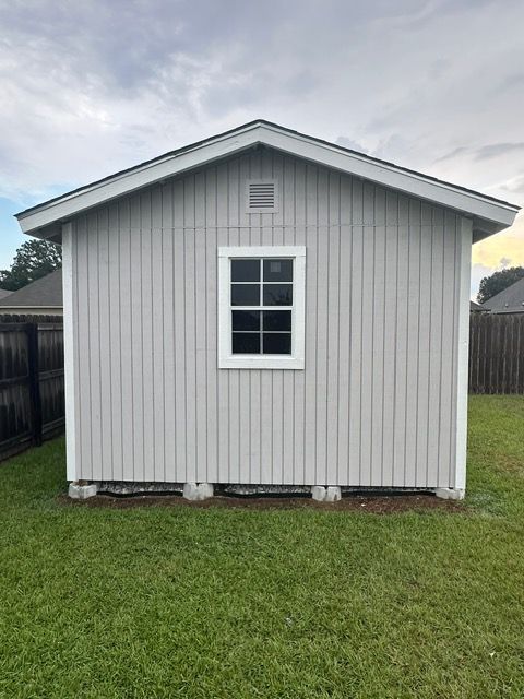Gray shed with white trim, small window, and gable roof, set on concrete blocks.