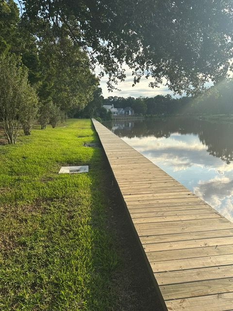 Wooden dock extends along a grassy shoreline into a calm body of water; trees in the background.