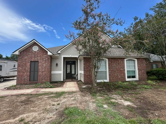 Brick and stucco house with a tree, lawn, and blue sky.