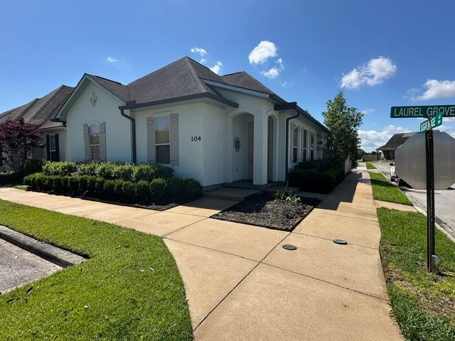 Exterior view of a light-colored house with a dark roof on a sunny day. Sidewalk and green lawn are in the foreground.