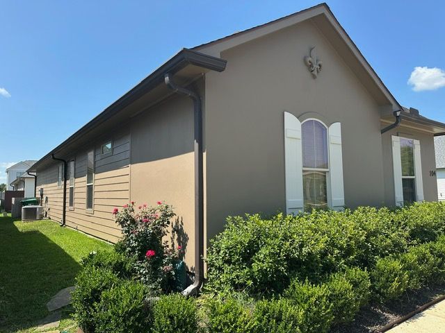 Brown house with brown gutters, shutters, and siding. Green bushes and grass are in the foreground.