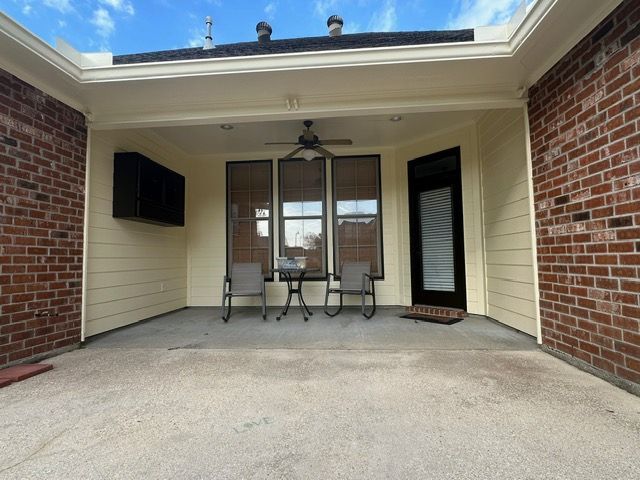 Covered patio with brick walls, tan siding, ceiling fan, and outdoor seating.