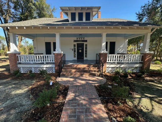 White house with porch and brick pathway leading to the front door.