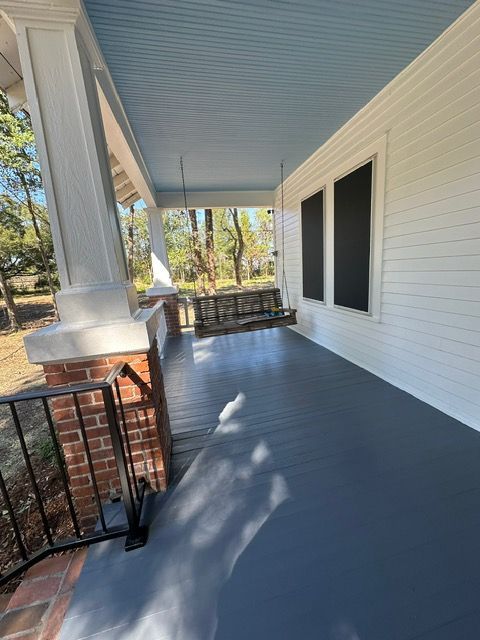 Covered porch with blue ceiling, gray floor, white siding, and black window screens.