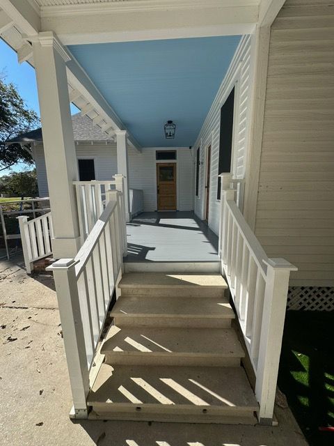 Exterior of a house with steps leading to a covered porch, blue ceiling, white railings and trim.