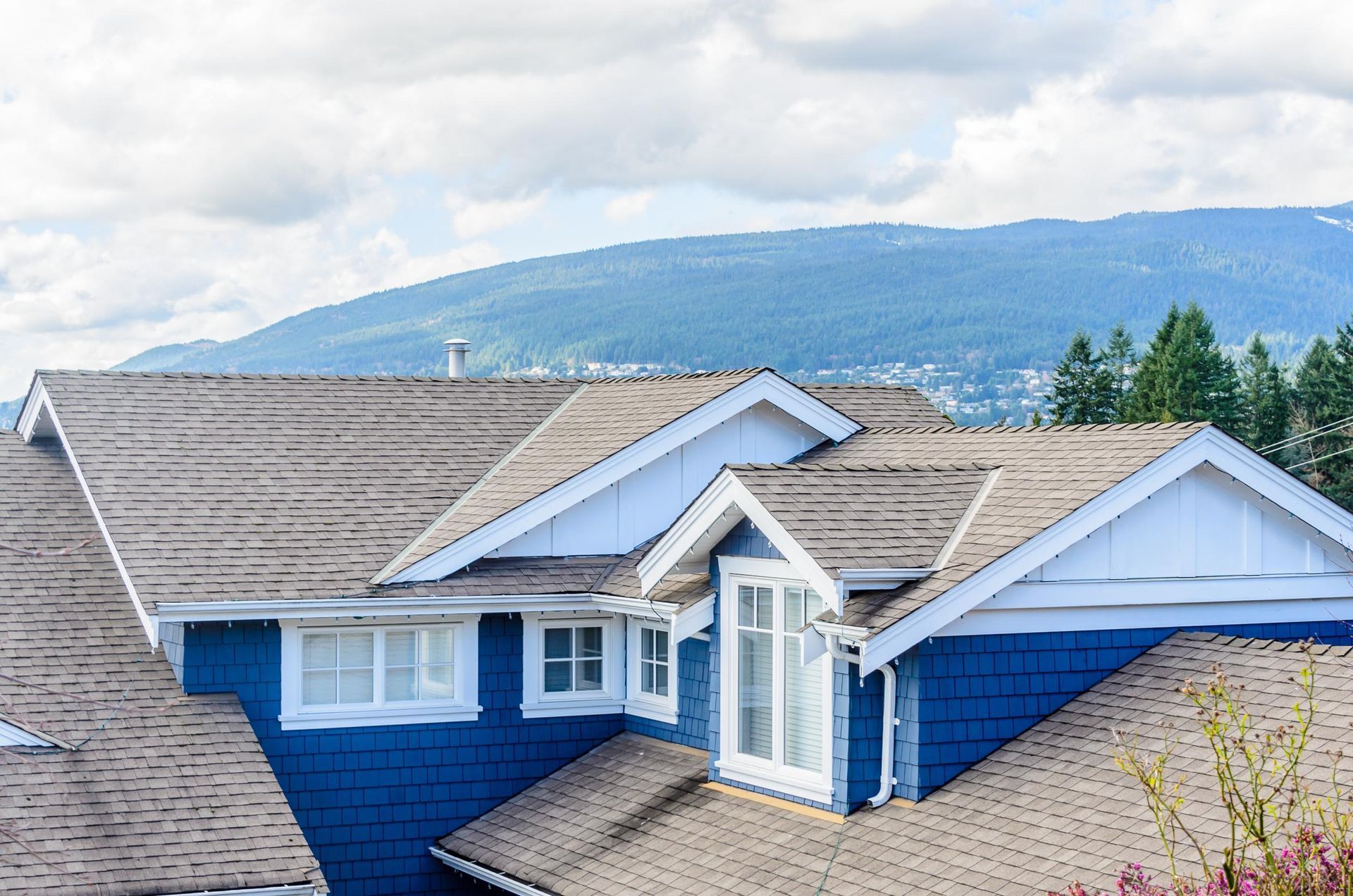 A blue and white house with a roof and mountains in the background.