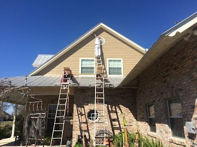 A man is standing on a ladder painting the side of a house.
