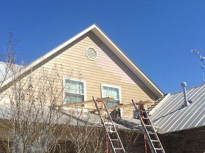 A man is standing on a ladder on the roof of a house.