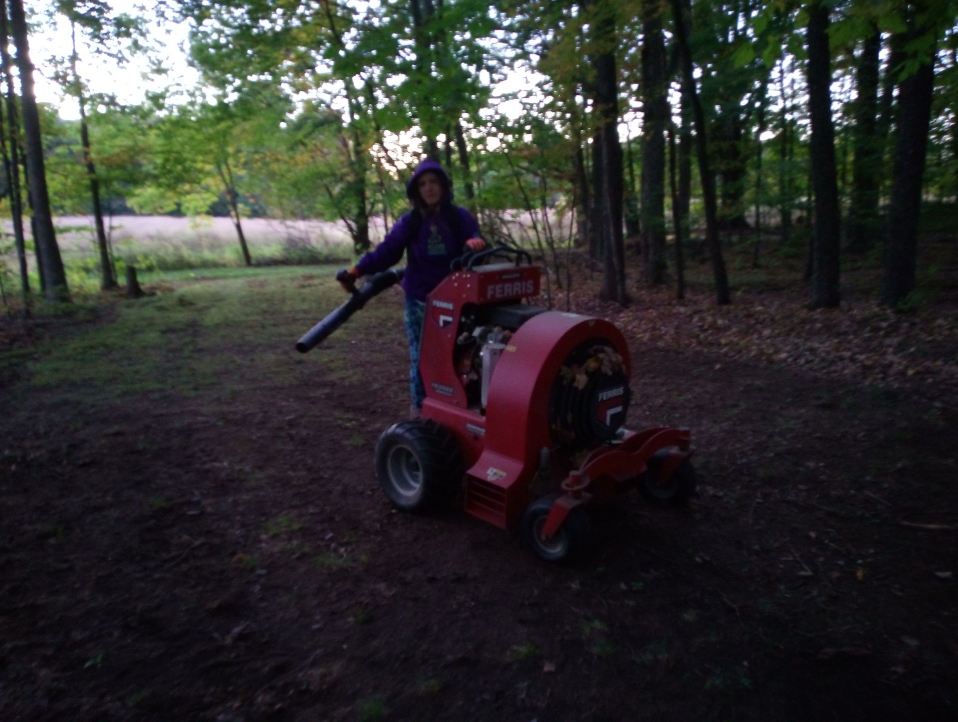 A person is riding a red lawn mower in the woods