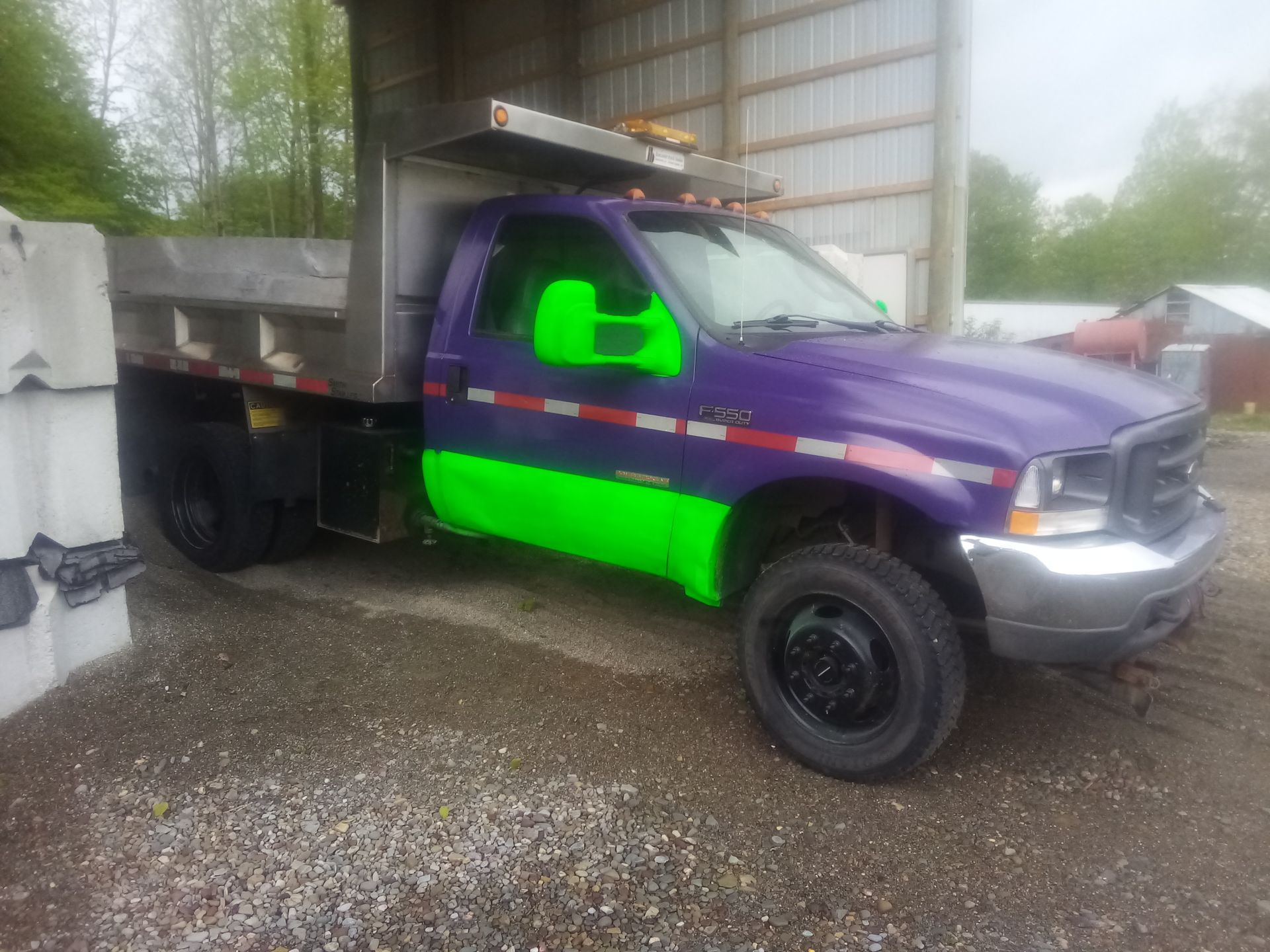 A purple and green dump truck is parked in a gravel lot.