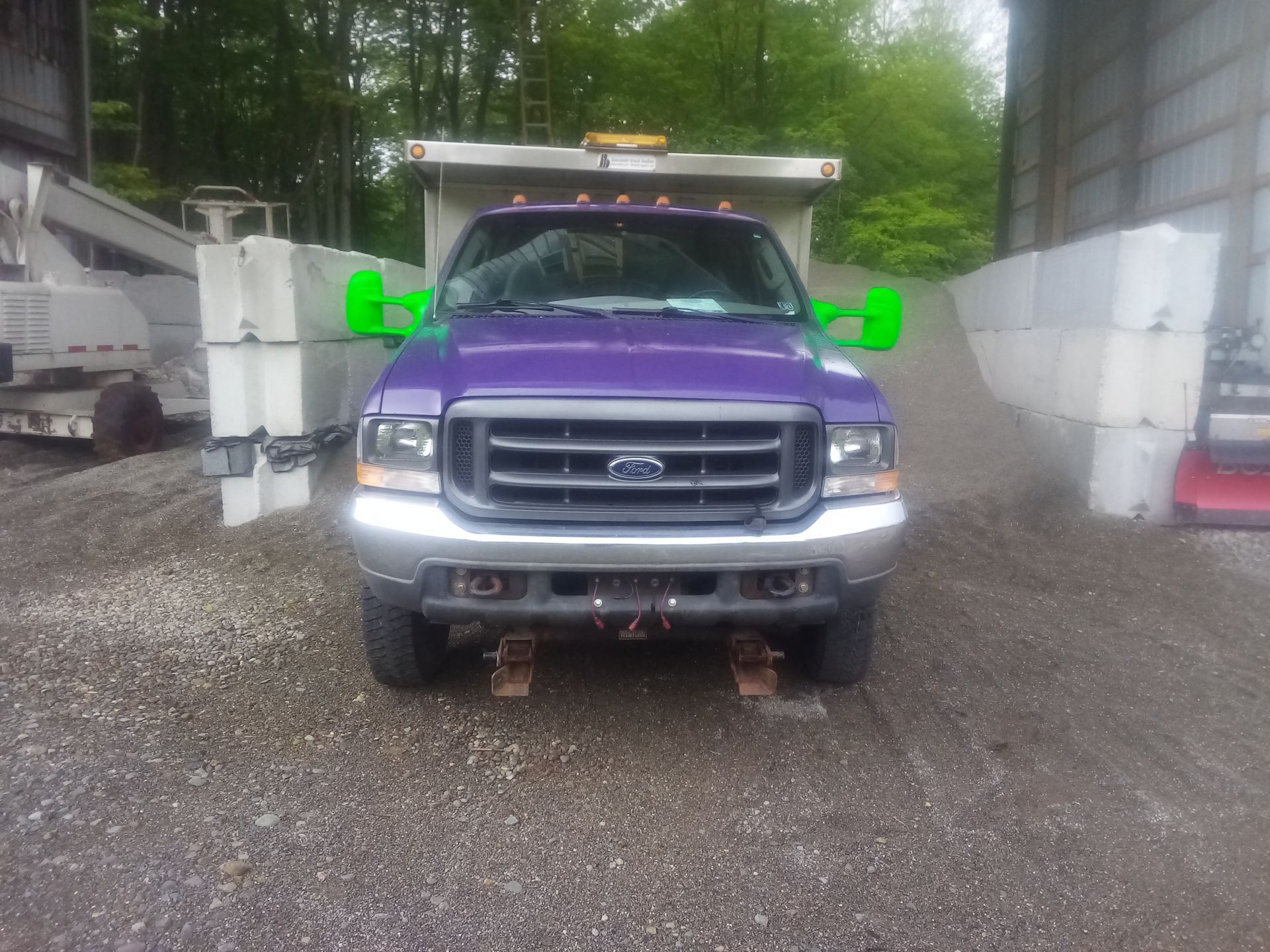 A purple truck with green mirrors is parked in a gravel lot.