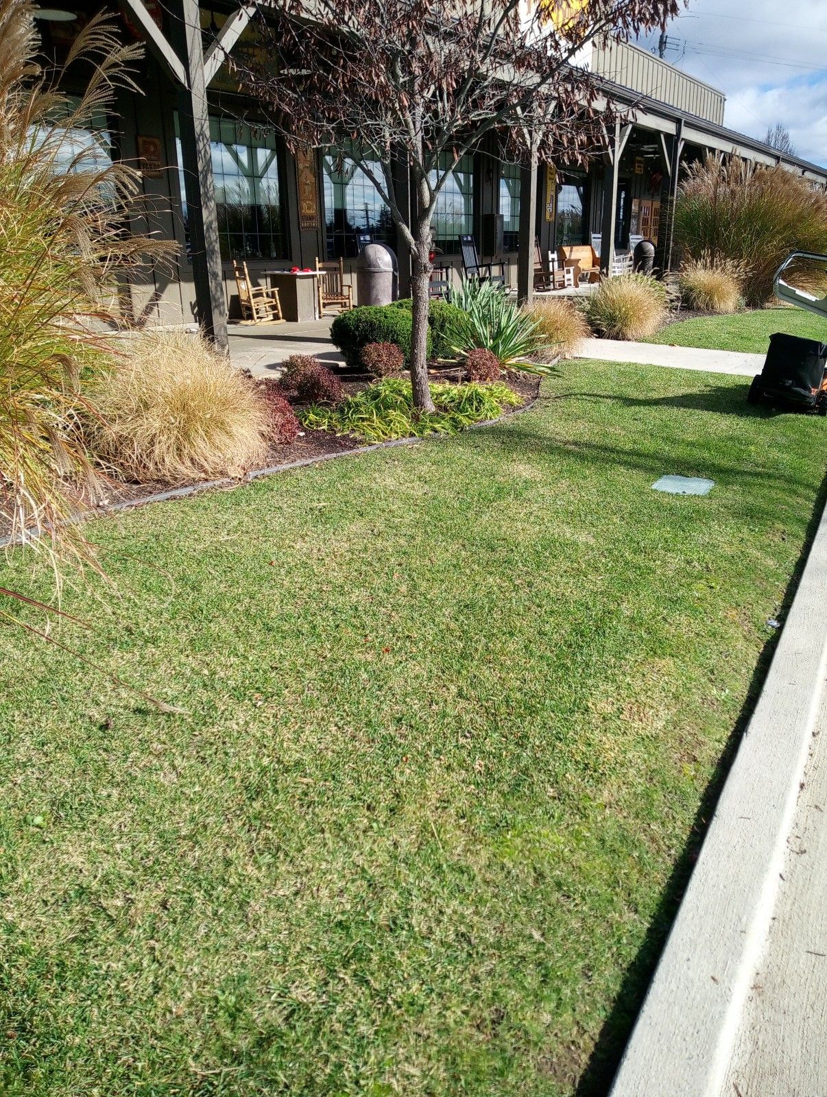 A lawn mower is cutting the grass in front of a building.