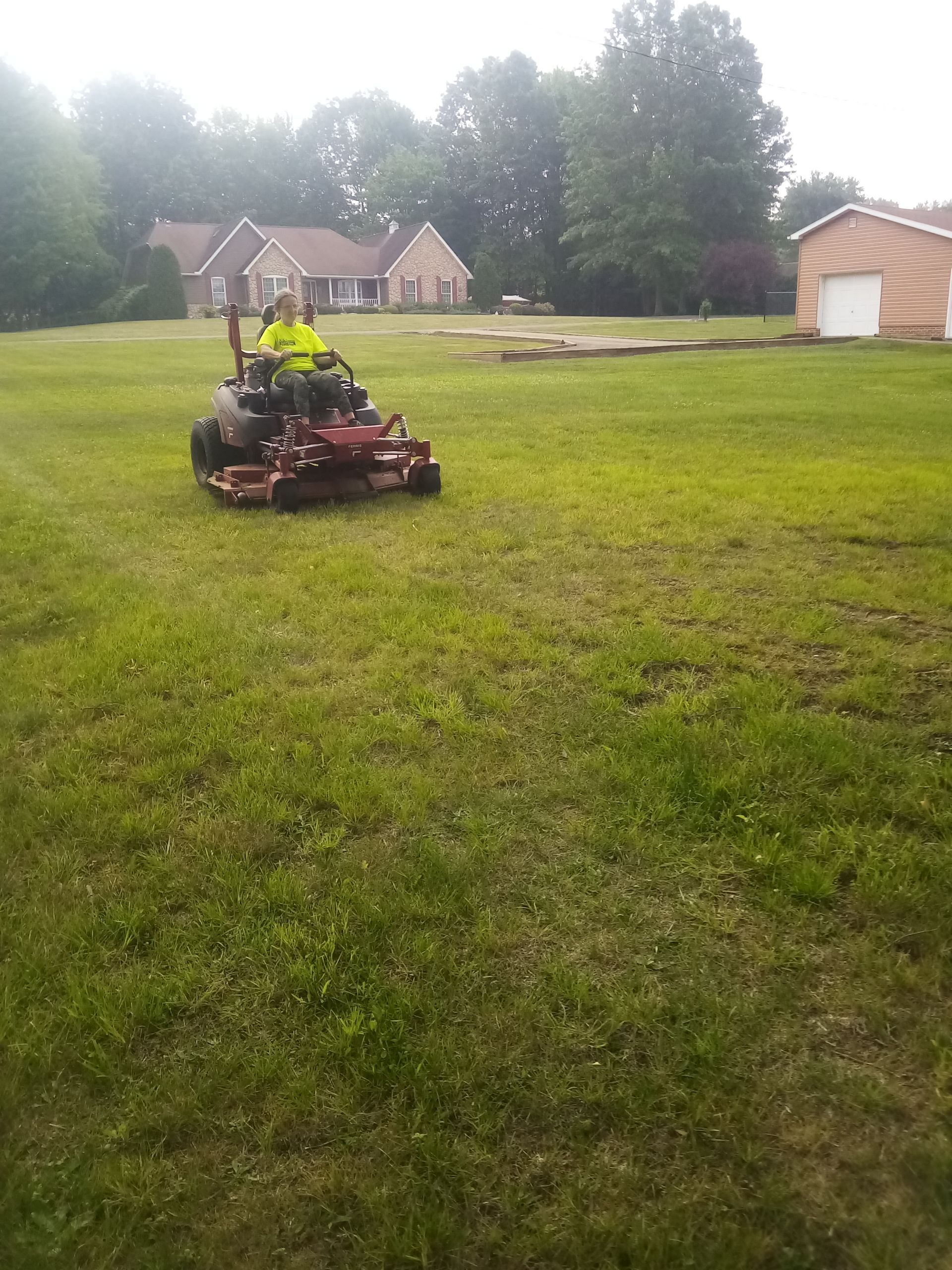 A man is riding a lawn mower through a lush green field.