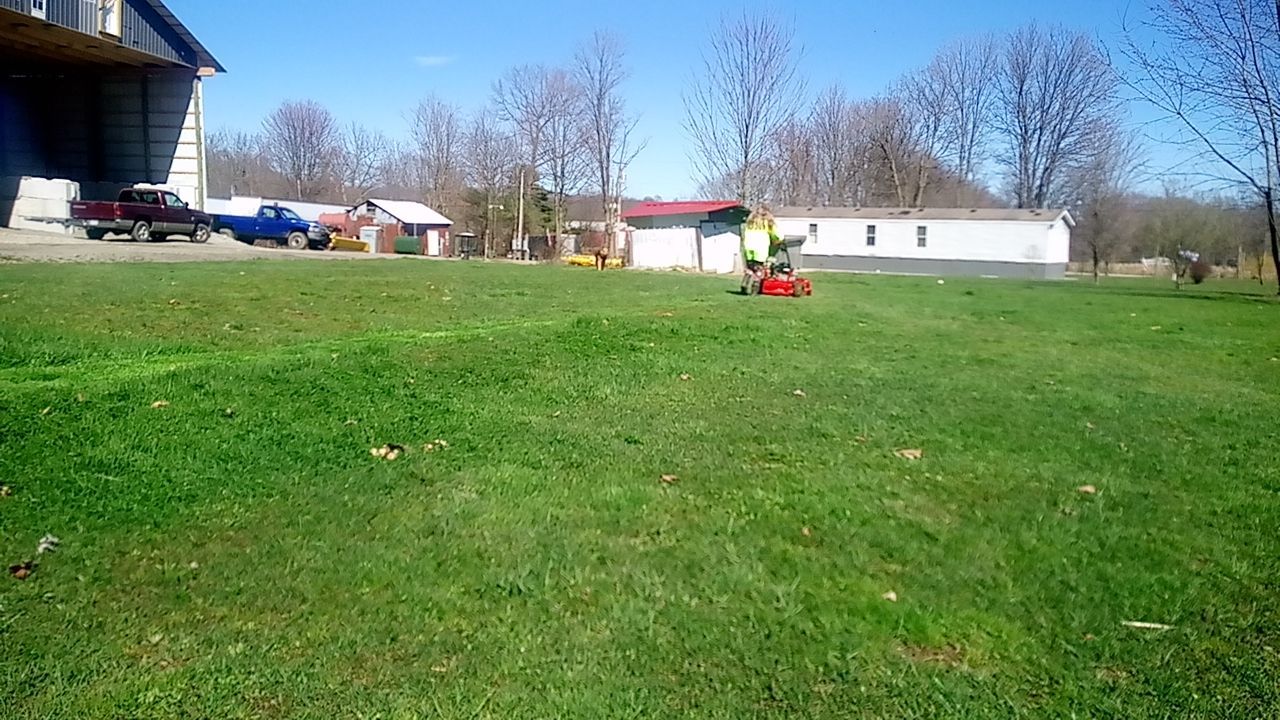 A person is mowing a lush green field with a red lawn mower.