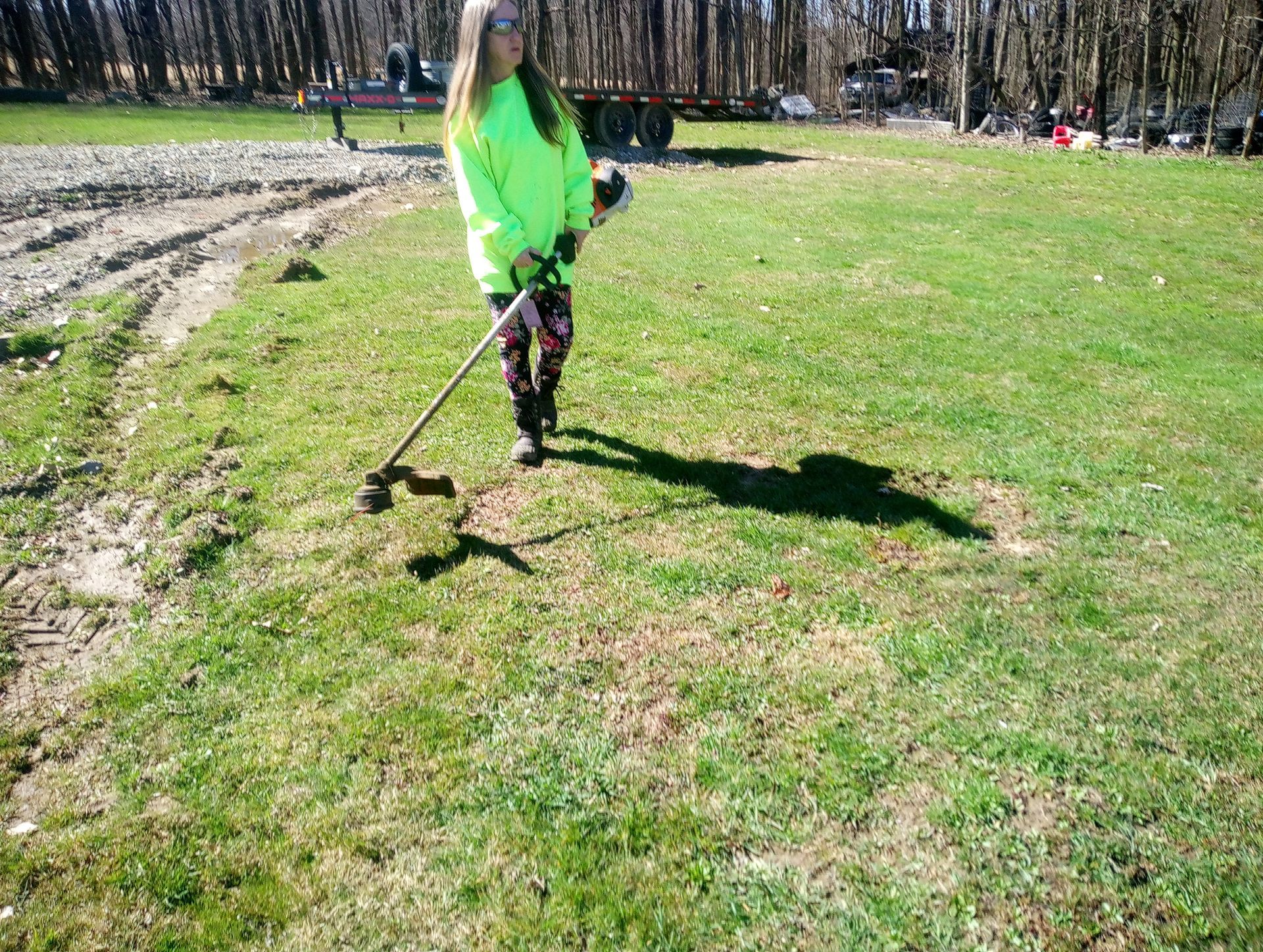 A woman is standing in a grassy field holding a weed wacker.