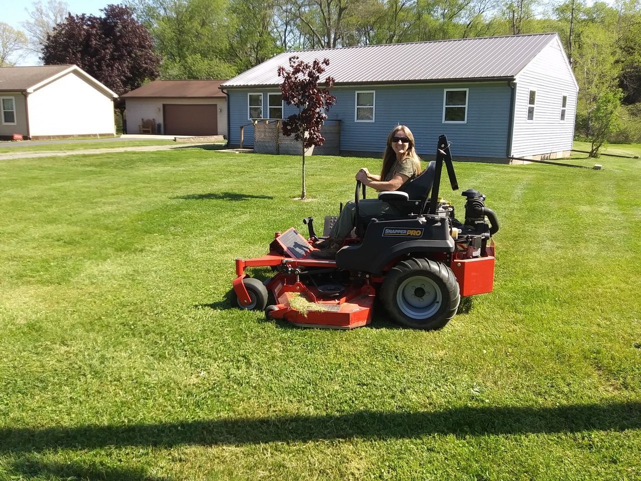 A woman is sitting on a lawn mower in front of a house