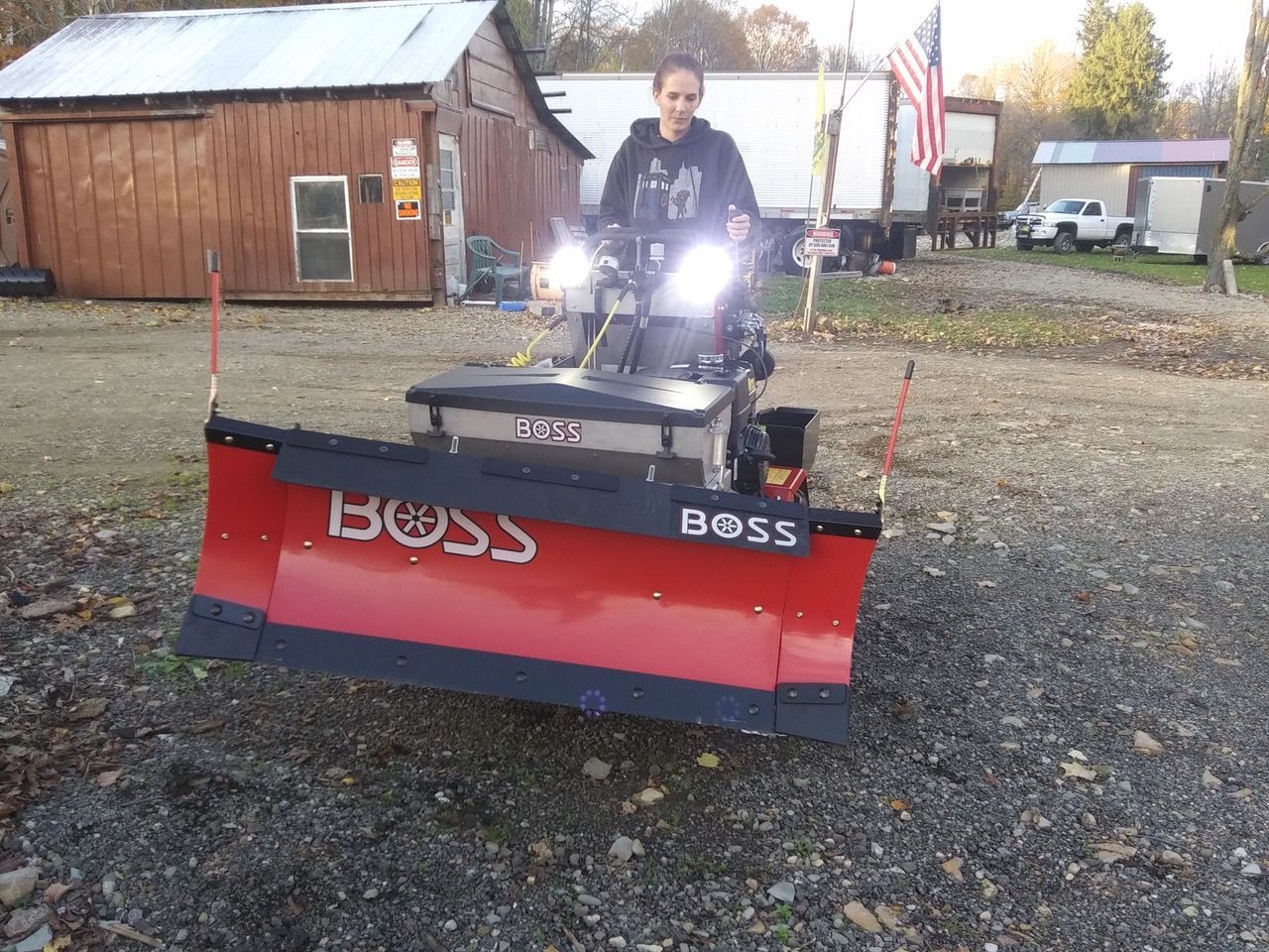 A woman is driving a boss snow plow on a gravel road