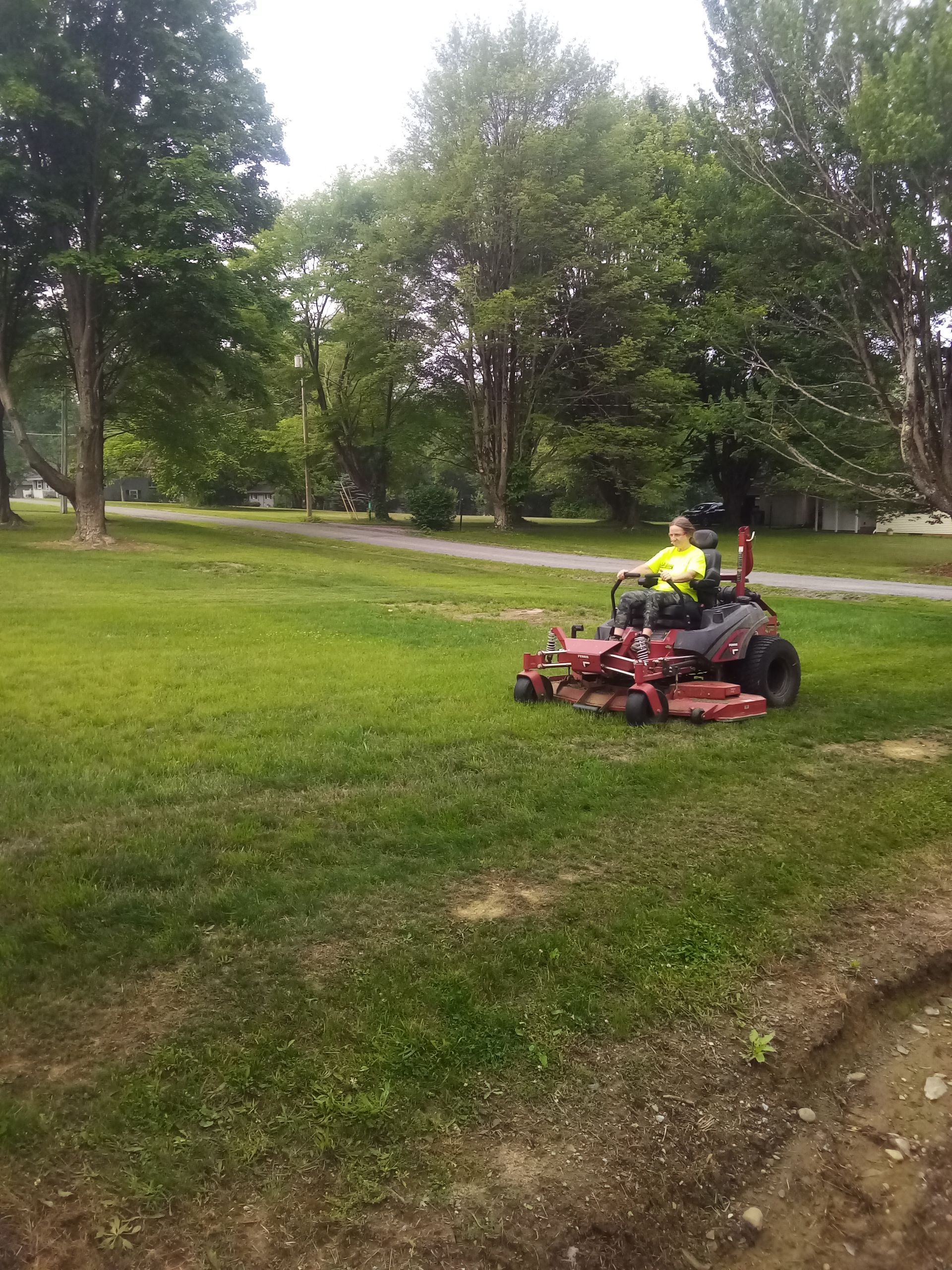 A woman is riding a lawn mower in a park.