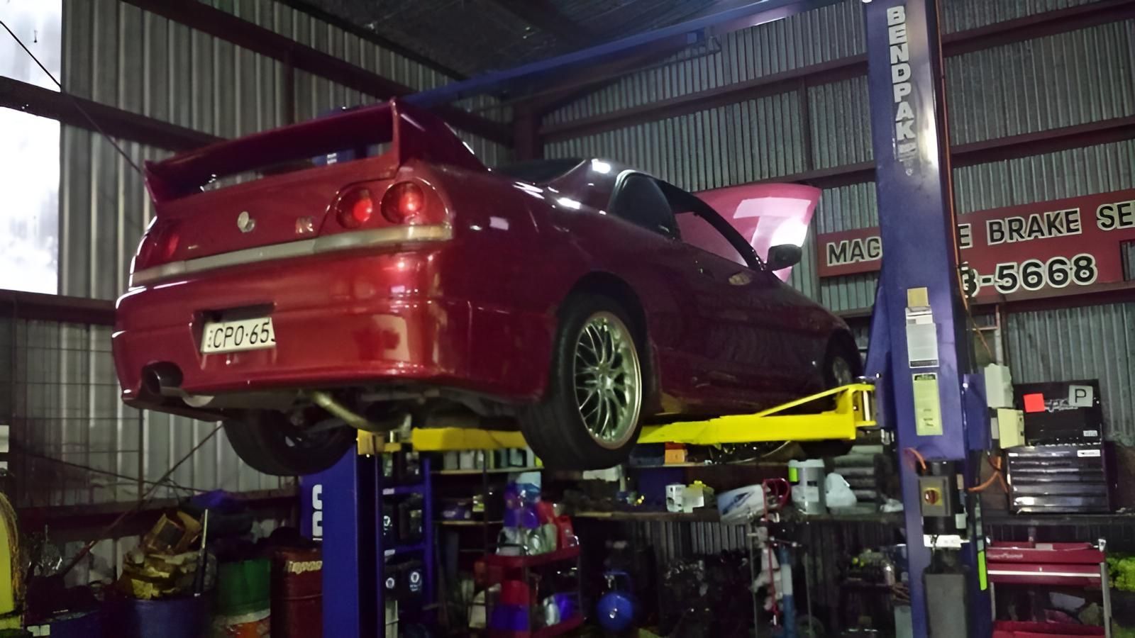 A Red Car is Sitting on a Lift in a Garage — Macquarie Brake & Automotive Services In Lake Cathie, NSW
