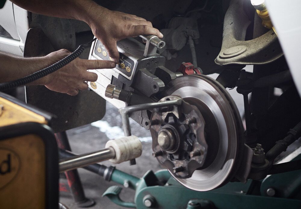 A Man is Working on a Brake Disc on a Car — Macquarie Brake & Automotive Services In Bonny Hills, NSW