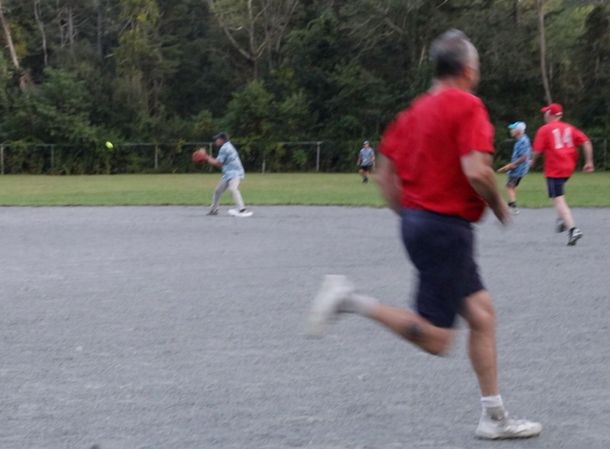 Baseball glove with ball on green grass, with blurred baseballs in the background.