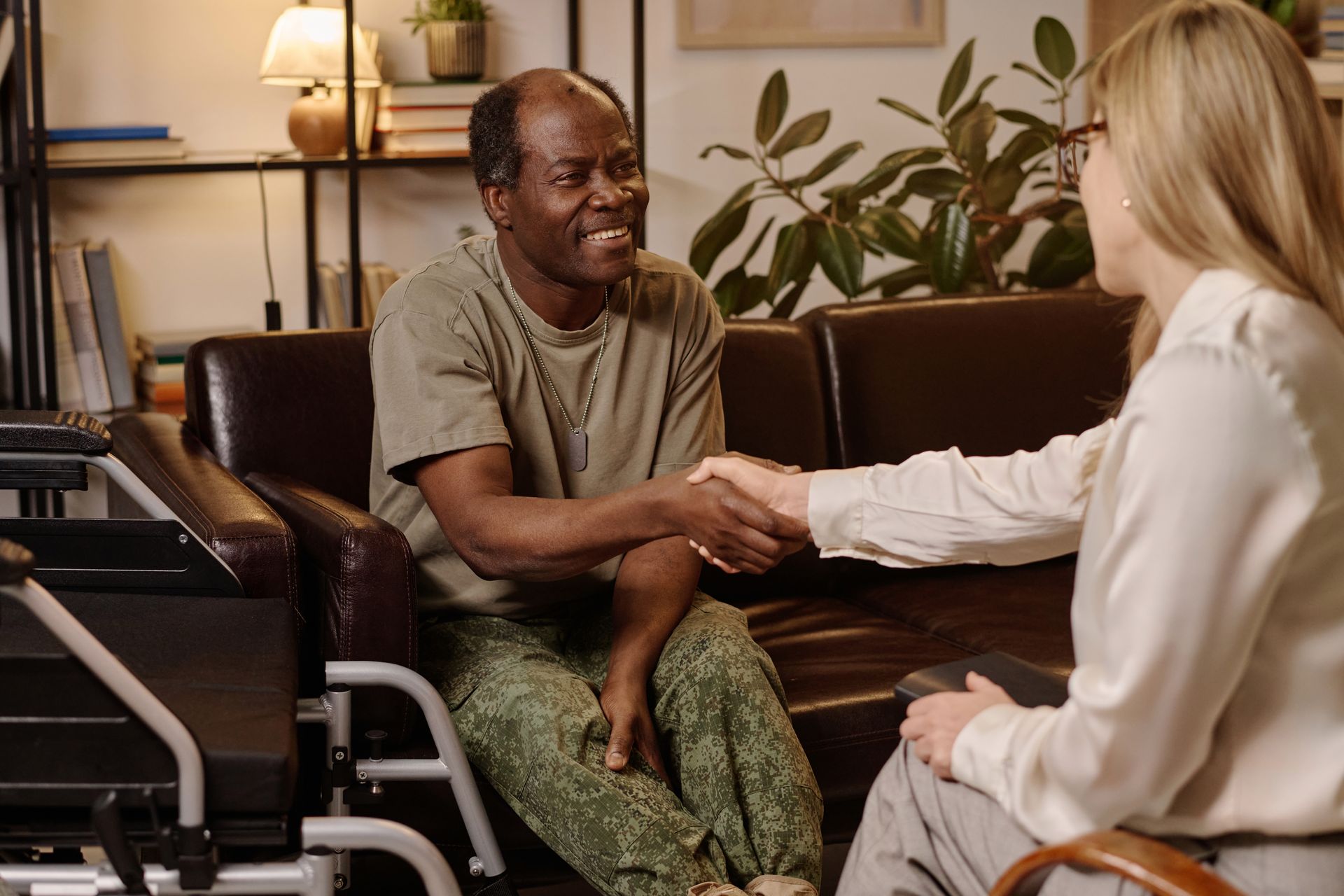 A person sitting in a wheelchair shakes hands with a professional in a warm, indoor setting.