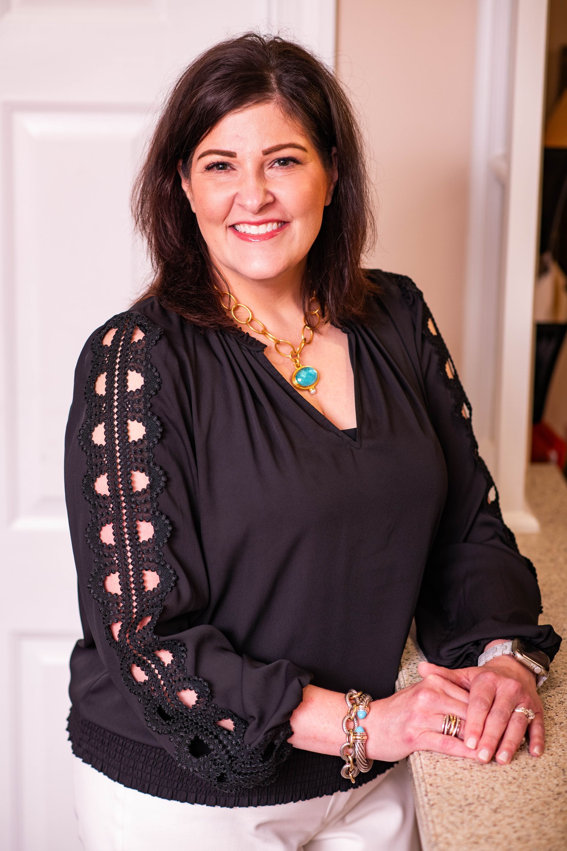 A woman in a black top and white pants is standing next to a door.